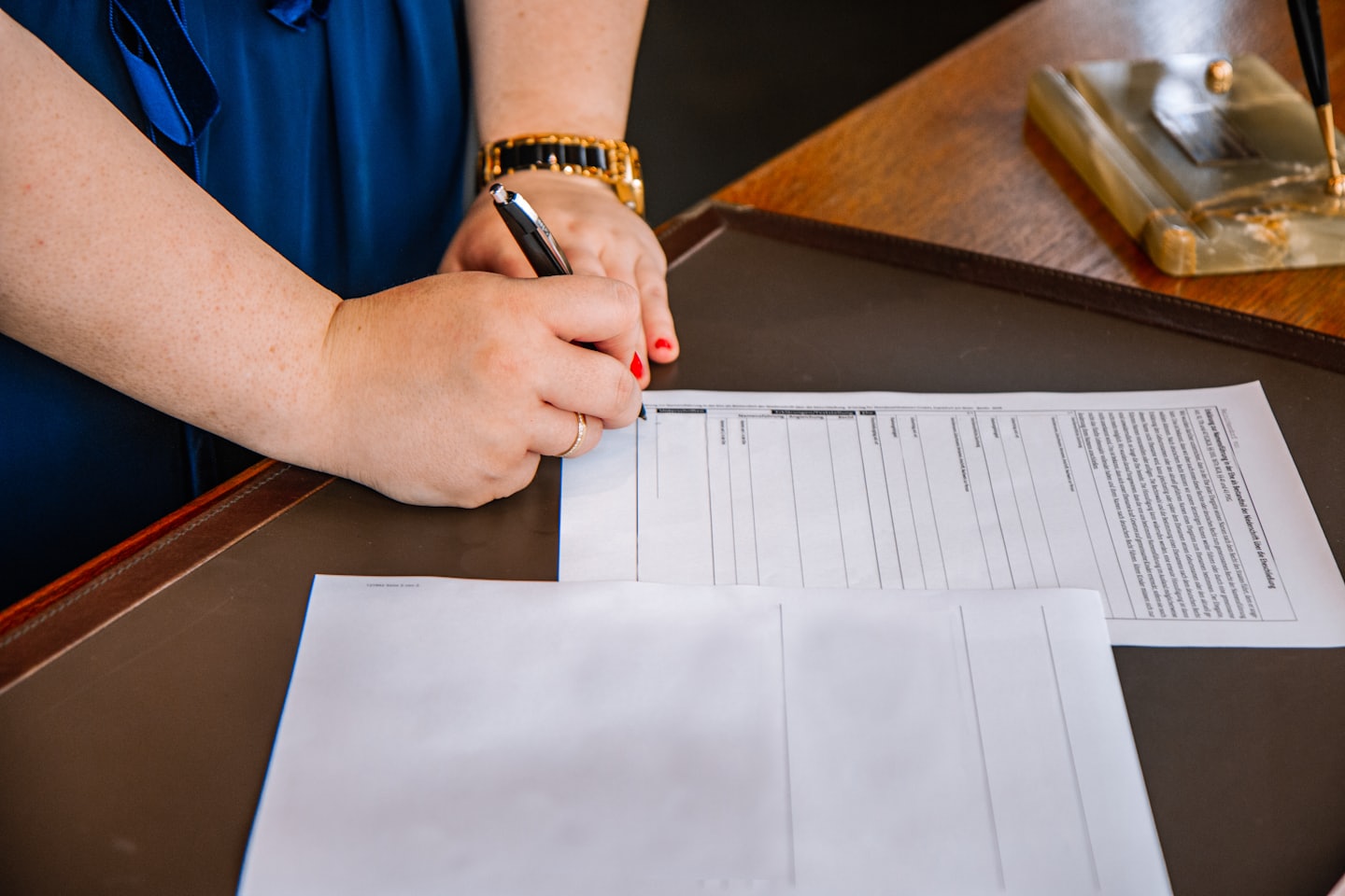 Hands signing a document at a leather-topped desk.